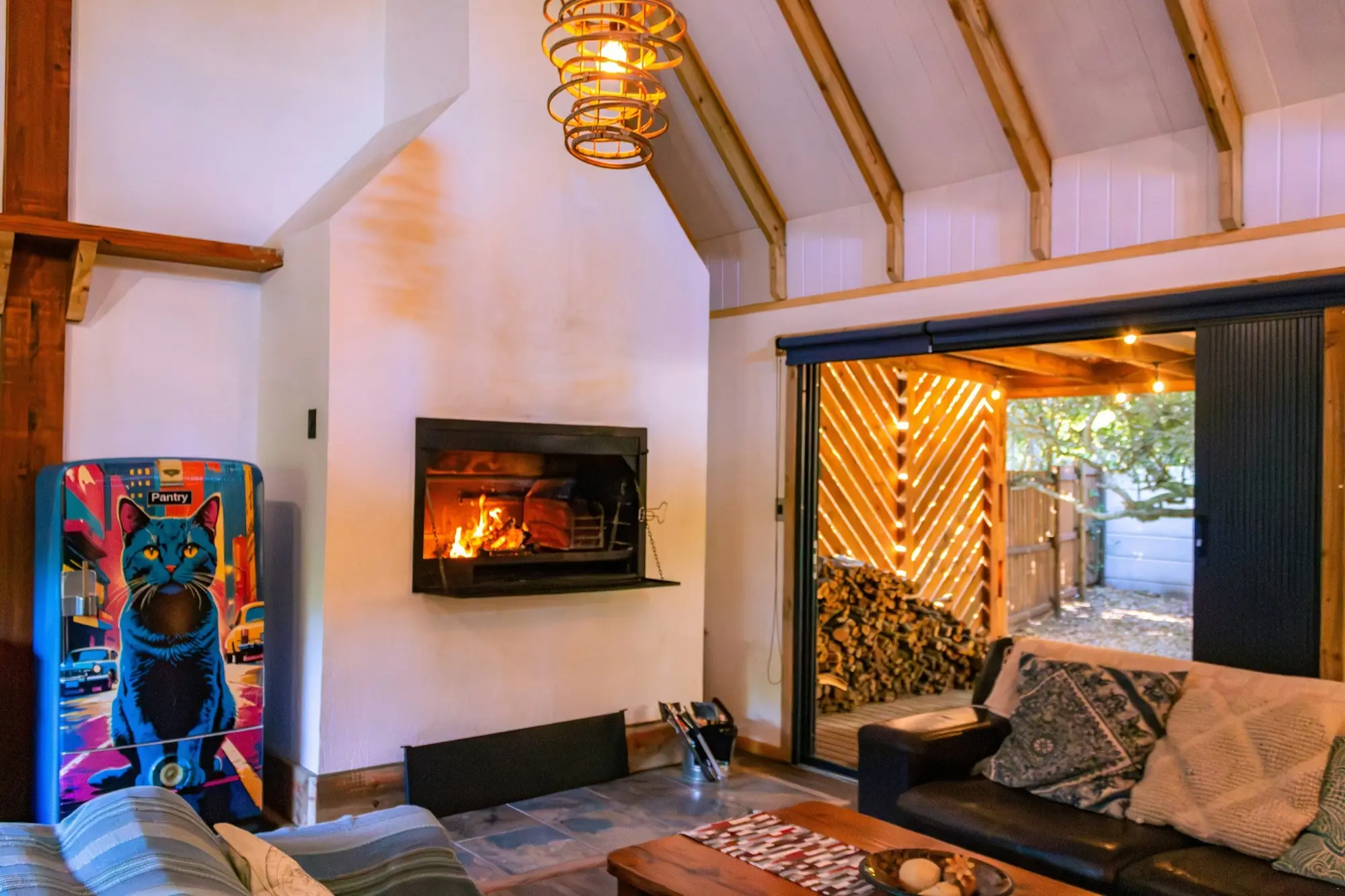 Wood-burning fireplace in the living room with the doors folded open to the forest