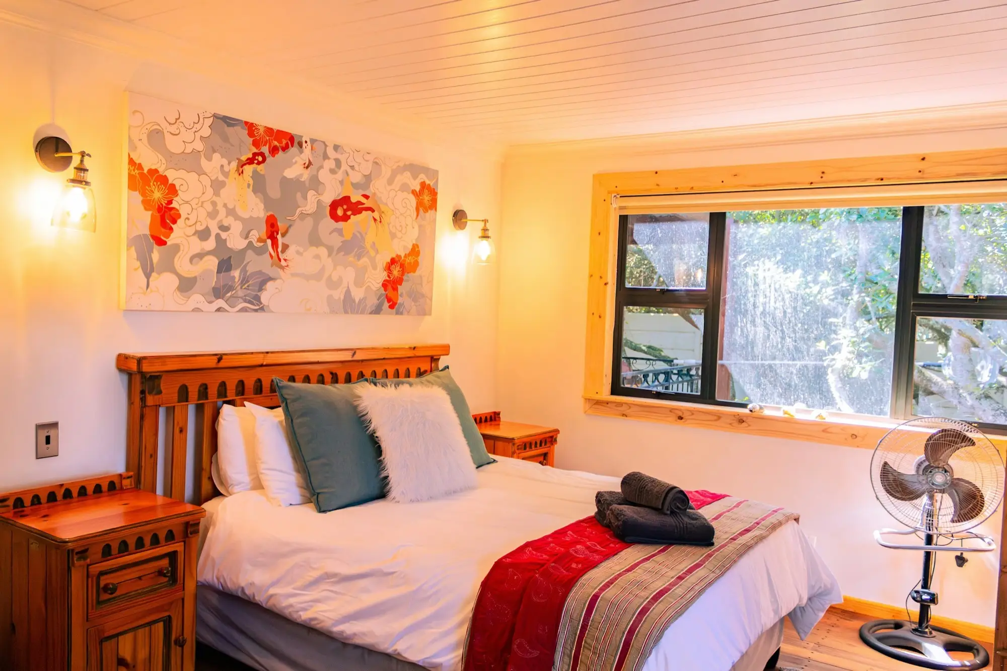 Queen bed in the master bedroom with folded towels and a window onto the forest
