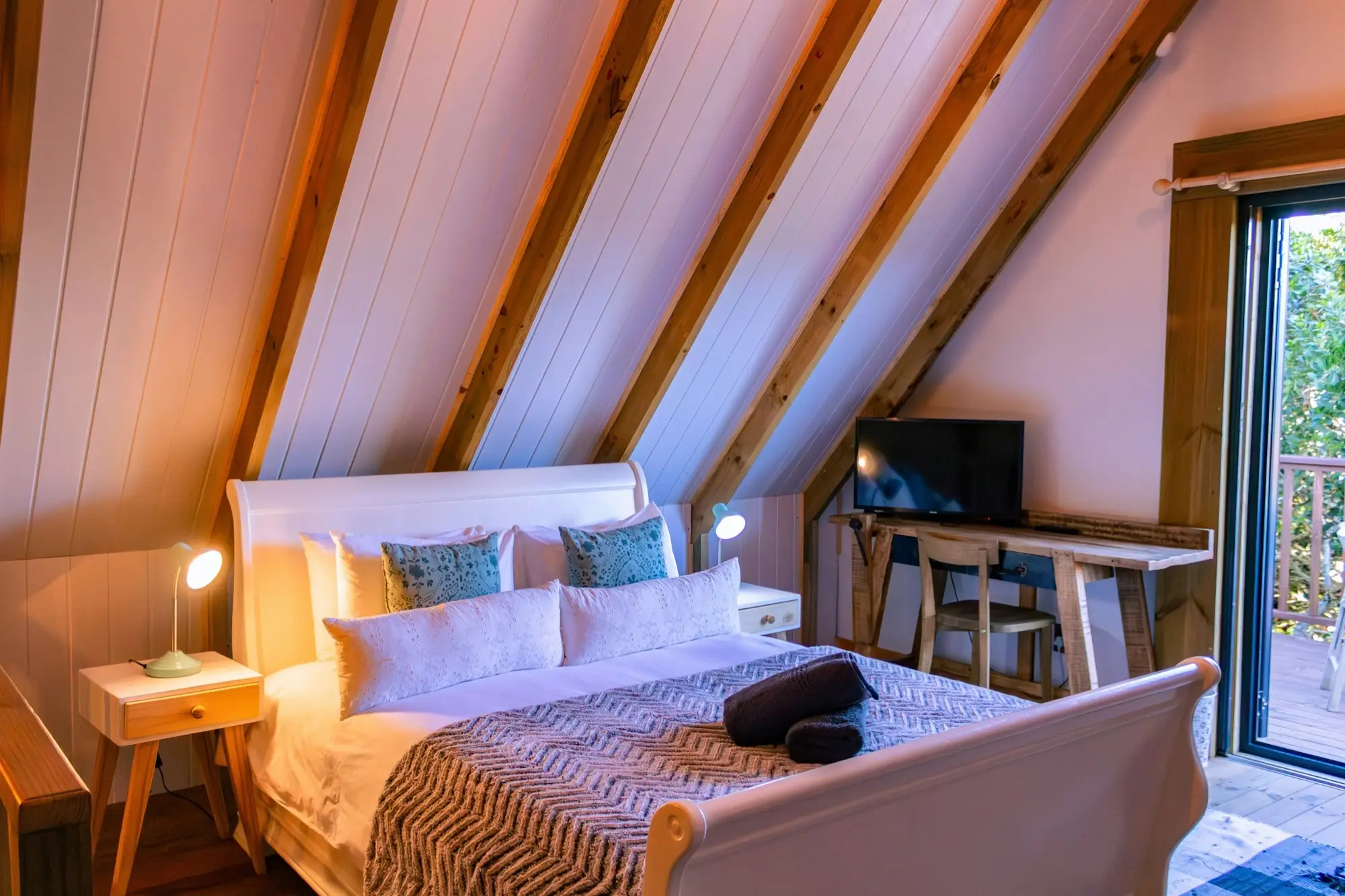 Loft bedroom with a sleigh bed, desk and television under the eaves