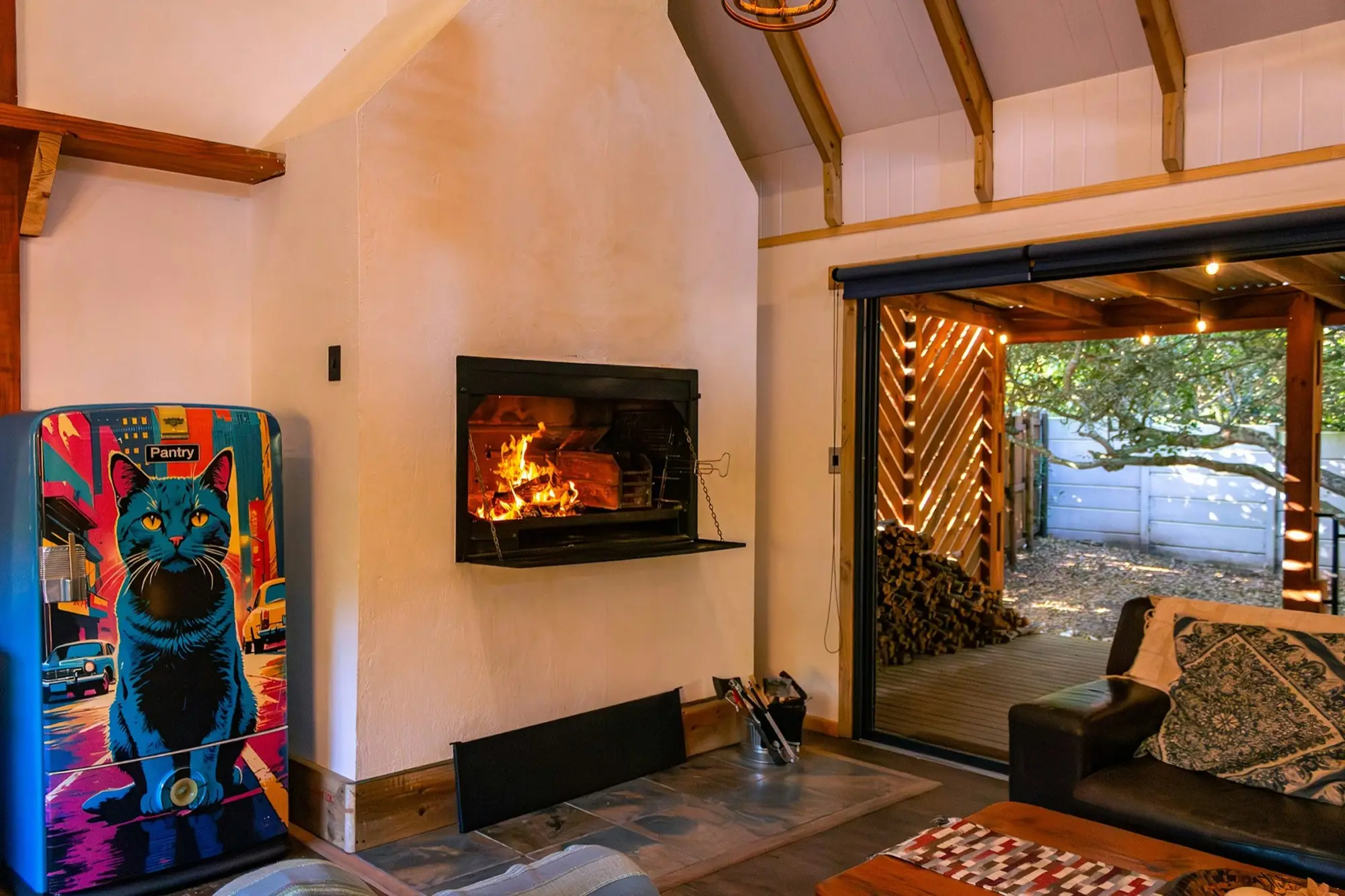Fire burning in the hearth with stacked firewood and the doors open to the trees